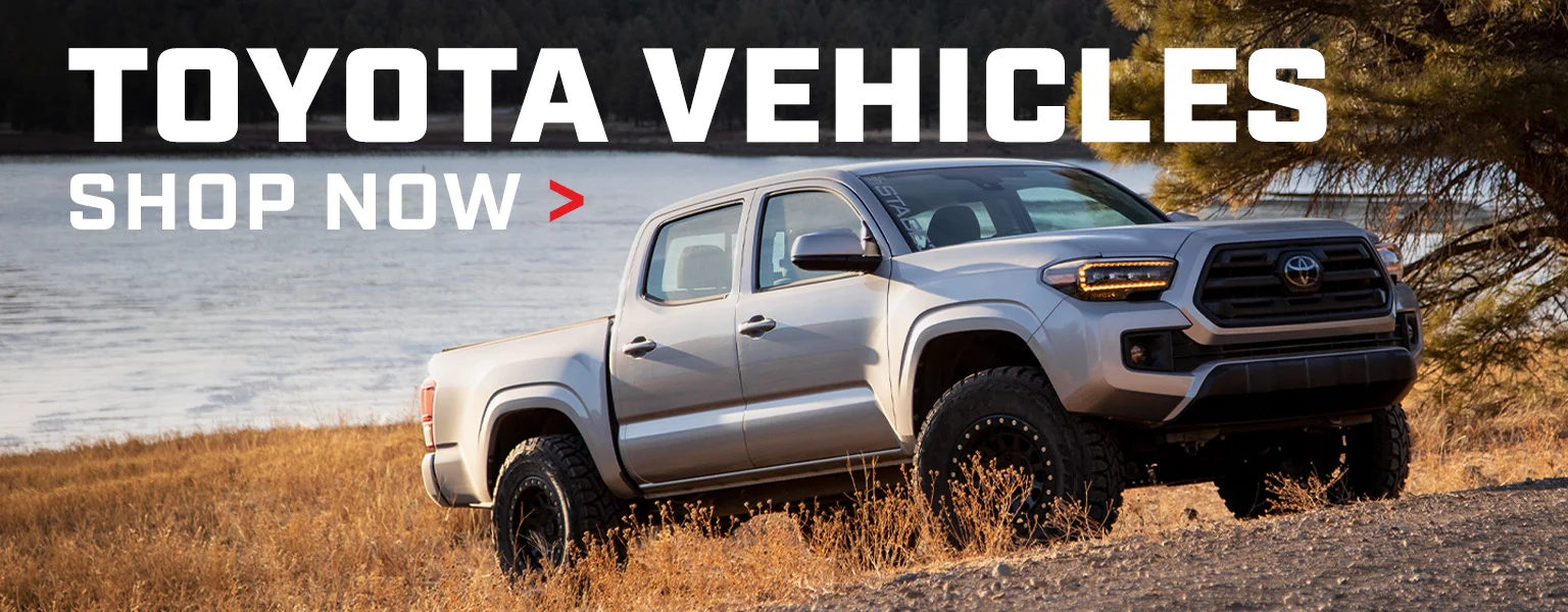 Shop Toyota Vehicles. Silver Toyota Tacoma on aftermarket wheels at the lakeside.